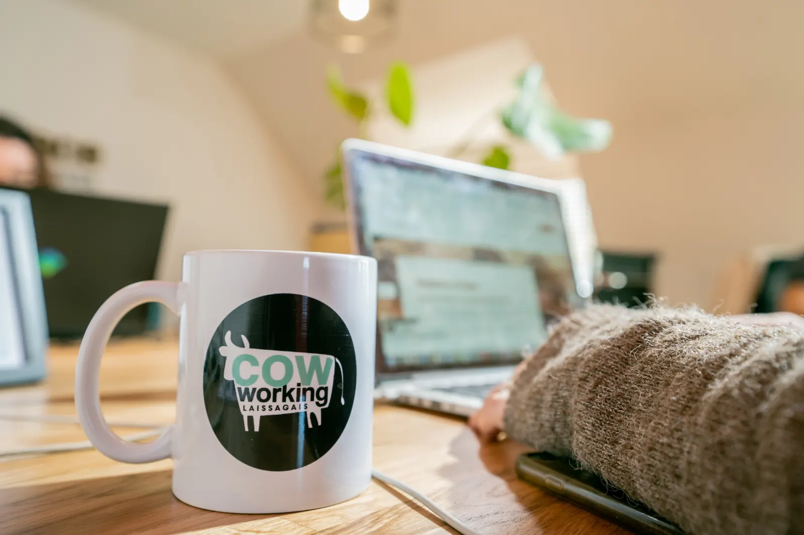 Mug Cow-working Laissagais posé sur un bureau à côté d'un ordinateur portable